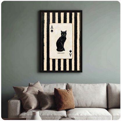 Framed artwork of a black cat inside an ace playing card above a sofa with muted cushions.