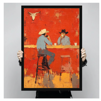 Person holding black framed cowboys at bar artwork against a plain pale background.