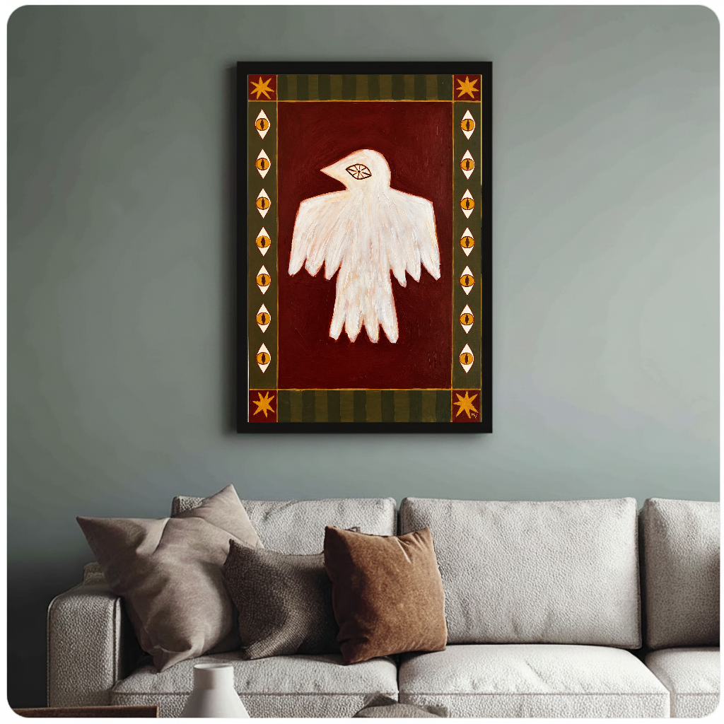 Framed folk bird with eyes painting above a sofa with muted cushions against a green-gray wall.