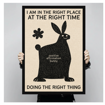 Framed artwork of a bunny with an encouraging affirmation held by a person against a pale backdrop.