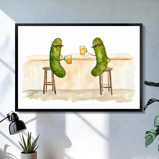 Black framed pickle friends beer toast canvas on a pale wall above a desk and plant.