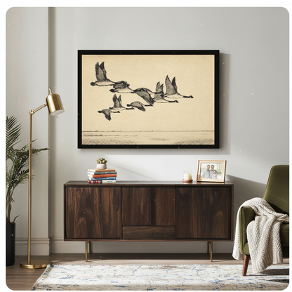 Framed flying geese over quiet water canvas above a wooden sideboard with books and a brass lamp.