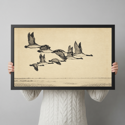 A person wearing a cream sweater holds black framed flying geese over quiet water canvas in both hands.