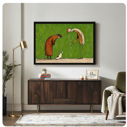Framed kind strangers small dog canvas above a wooden sideboard beside books and an angled brass lamp.