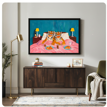 Framed tigers enjoy pizza in bed canvas above a wooden sideboard beside books and an angled brass lamp.