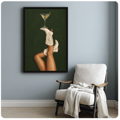 Framed cowgirl boots martini balance canvas beside a pale reading chair on a blue gray wall.