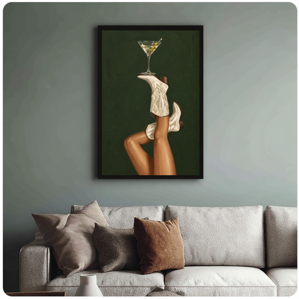 Framed cowgirl boots martini balance canvas above a neutral sofa with cushions against a muted wall.