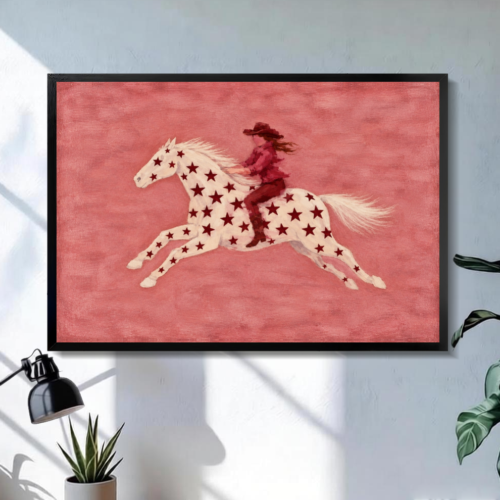 Black framed star horse pink rider canvas on a pale wall above a desk and plant.