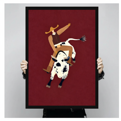 Framed burgundy rodeo rider canvas held by a person against a light neutral background.