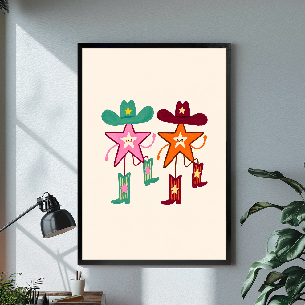 Black framed two cowboy stars canvas on a pale wall above a desk and plant.