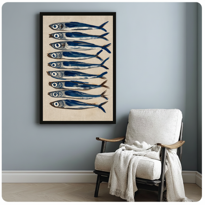 Framed nine blue sardines canvas beside a pale reading chair on a blue gray wall.