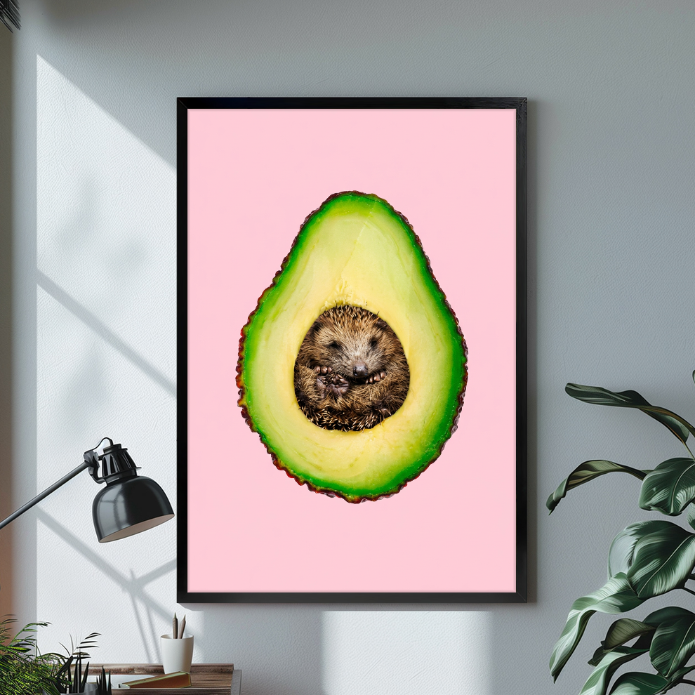 Black framed avocado hedgehog canvas on a pale wall above a desk and plant.