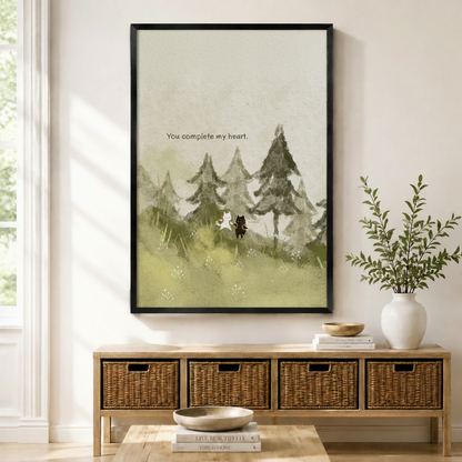 Black framed watercolor you complete my heart white cat and black dog canvas art with a small white cat and black dog standing together on a misty pine forest slope forming a heart shape beside the hand-lettered quote you complete my heart in soft sage green tones, displayed on a light wall above a wooden rattan storage console with a white vase of greenery