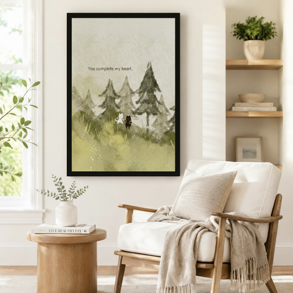Black framed watercolor white cat and black dog in a pine forest canvas art showing a little cat and dog standing close together on a soft green hillside among misty fir trees with the you complete my heart quote in gentle sage watercolor, displayed on a white wall beside a light upholstered wooden armchair draped with a cream fringed throw blanket near a shelf of plants