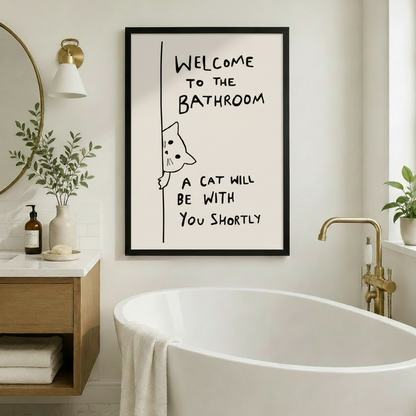 Framed humorous cat peeking wall art with bathroom quote displayed beside a freestanding soaking tub in a warm Scandinavian bathroom with gold sconce and round mirror
