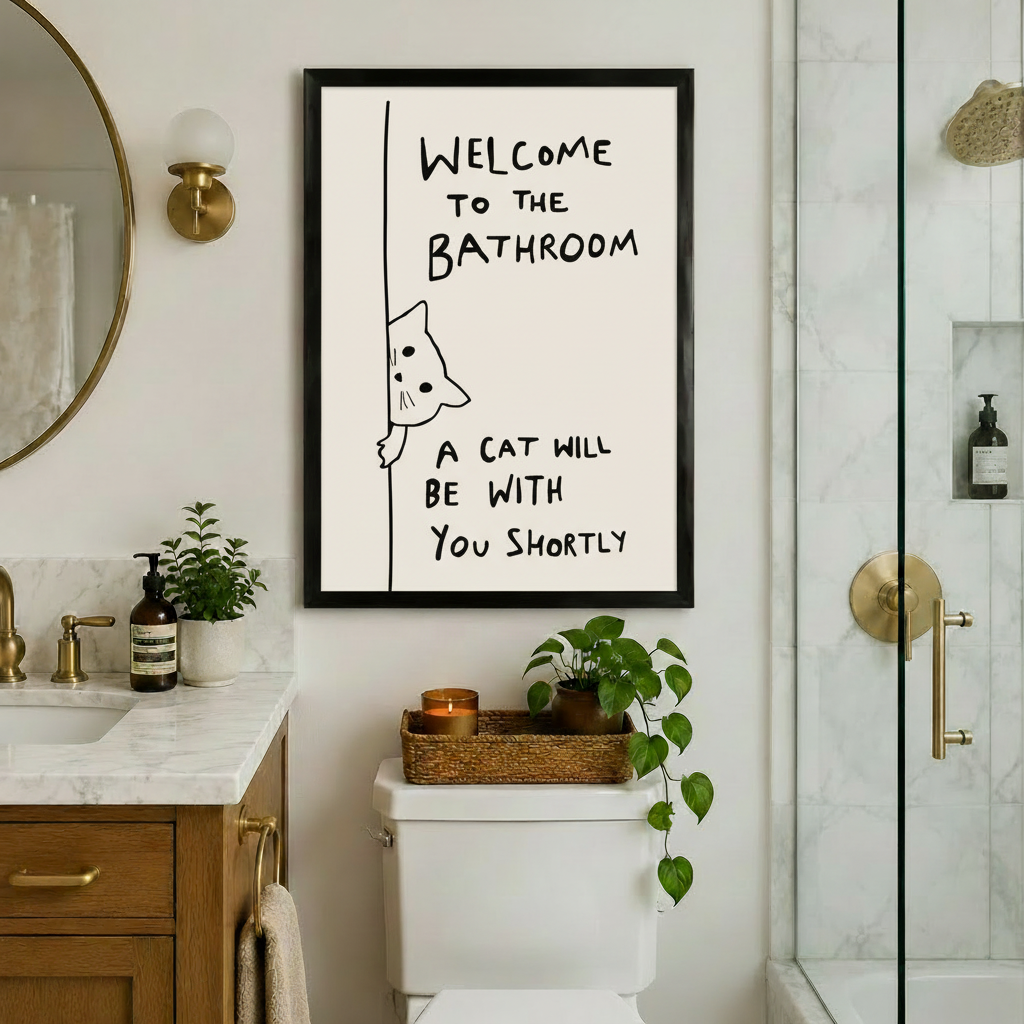 Black-framed witty cat bathroom quote art print hung above a toilet in a luxury bathroom with gold fixtures, marble countertop, and glass shower enclosure
