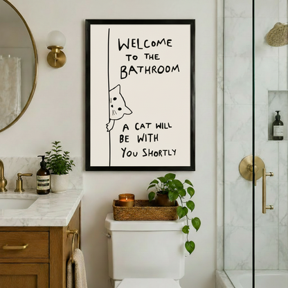 Black-framed witty cat bathroom quote art print hung above a toilet in a luxury bathroom with gold fixtures, marble countertop, and glass shower enclosure