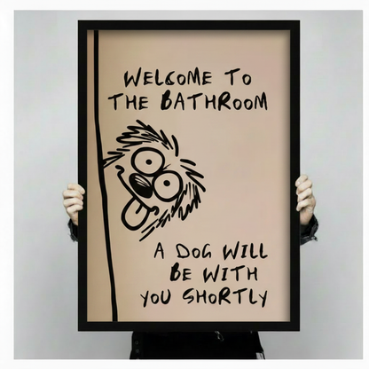 Person holding large black framed funny dog bathroom wall art print with welcome to the bathroom a dog will be with you shortly handwritten quote on beige background