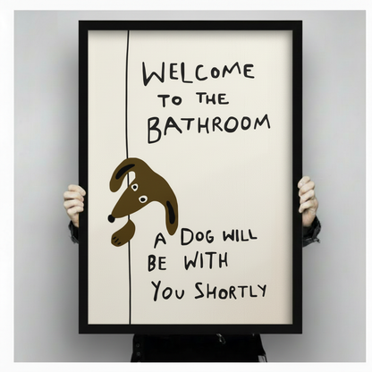 Person holding large black framed funny dog bathroom wall art print with welcome to the bathroom a dog will be with you shortly quote