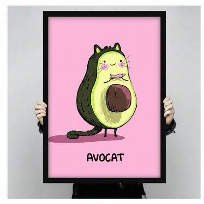 Hands holding a large black framed whimsical Avocat avocado cat canvas art print with a plump dark green avocado-shaped cartoon cat with tiny pointed ears blushing cheeks long white whiskers a small fish in its mouth a curling green tail and a round brown pit belly on bird-like feet above bold black Avocat text on a vivid bubblegum pink background