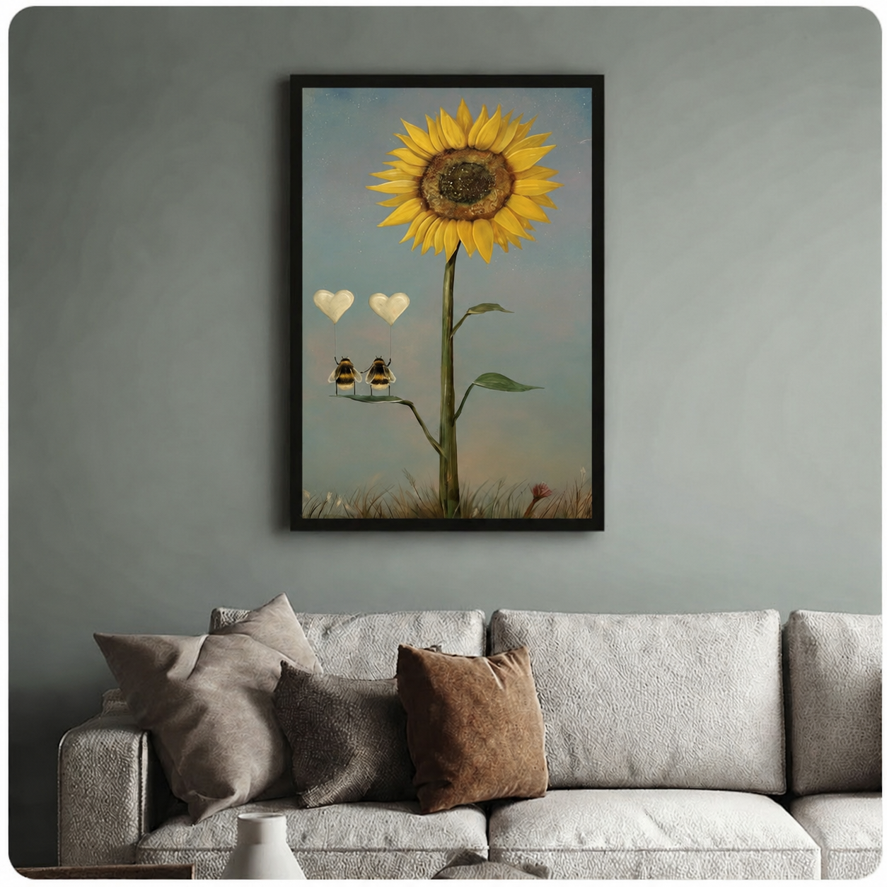 Whimsical framed poster of two bees perched on a sunflower stem with floating heart balloons, hung above a neutral linen sofa