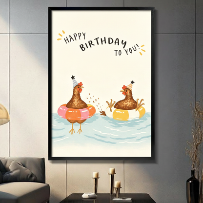 Black framed whimsical happy birthday chickens in pool floats canvas art with two brown hens wearing party hats splashing in pink and yellow swim rings in light blue water beneath a hand-lettered happy birthday to you quote on a cream background, displayed on a dark gray tile wall above a black table with candlesticks beside a gray sofa