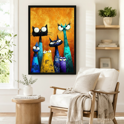 Black framed whimsical colorful cat family canvas art showing five quirky cats of varying heights in black teal blue yellow and purple with oversized expressive eyes and long whiskers in bold textured oil-paint style on a warm golden amber floral-patterned background, displayed beside a white linen armchair in a cozy reading nook
