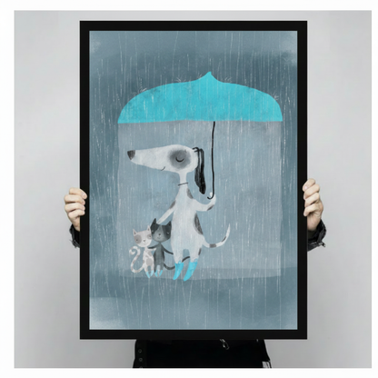 Person holding a large vertical black framed whimsical dog with umbrella and cats canvas art print showing a white dog in teal rain boots holding a blue umbrella with its tail to shelter a white kitten and a black and white kitten in the rain on a gray-blue background against a light gray studio backdrop