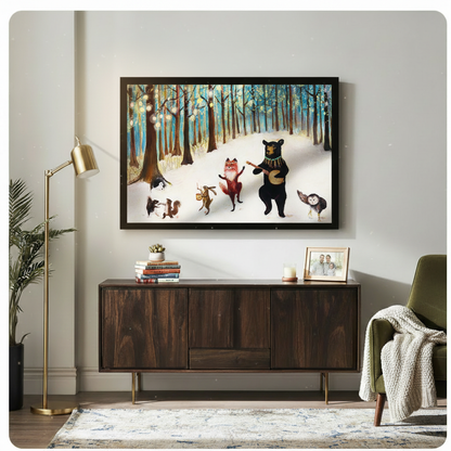 Black framed whimsical fairy tale forest animals music party horizontal canvas art with bear fox rabbit squirrel and owl in snowy teal forest above a dark walnut sideboard with stacked books and a succulent beside a brass floor lamp and olive green armchair