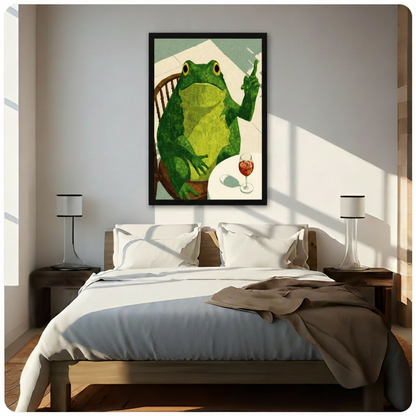 Black framed humorous frog sitting at a table with wine canvas art featuring a plump green frog on a Windsor chair raising a finger beside a glass of red spritz on a sage green background, hung above a wooden bed frame in a sun-drenched minimalist bedroom with crisp white linen bedding and matching cylindrical nightstand lamps