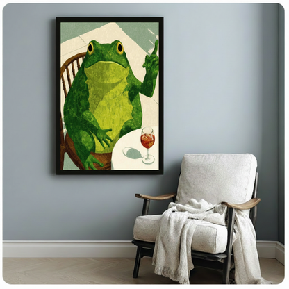 Black framed vintage-style frog with wine canvas art showing a cheerful green frog on a Windsor chair raising a finger beside a glass of red spritz on a white table with a linen-textured sage green background, displayed on a soft blue-gray wall beside a black-framed upholstered armchair draped with a cream knit throw blanket