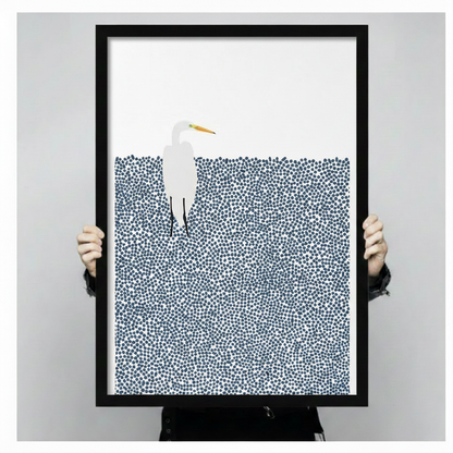 Person holding a large black framed minimalist white egret in pointillist navy blue water art print showing print size scale and fine dot texture detail