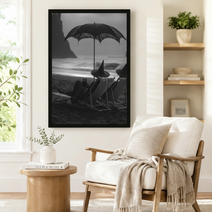 Black and white framed art print featuring witches and a black cat on a stormy seashore, styled beside a linen armchair in a cozy reading nook