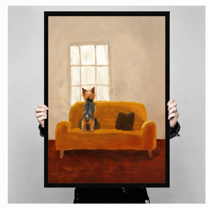 Both hands holding large framed Yorkshire Terrier print, full artwork view of small dog sitting alone on mustard yellow sofa facing a glowing window in warm oil painting style
