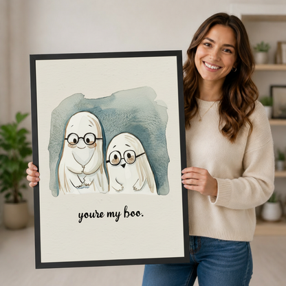 Smiling woman holding large You're My Boo ghost couple watercolor framed art print in black frame, demonstrating print size and artwork detail