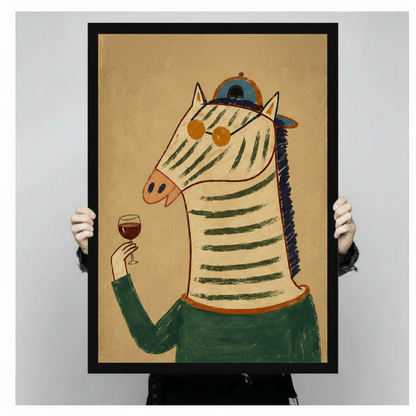 Two hands holding large black framed canvas print of retro zebra in green sweater and teal cap raising a red wine glass, warm antique kraft background against light gray studio backdrop